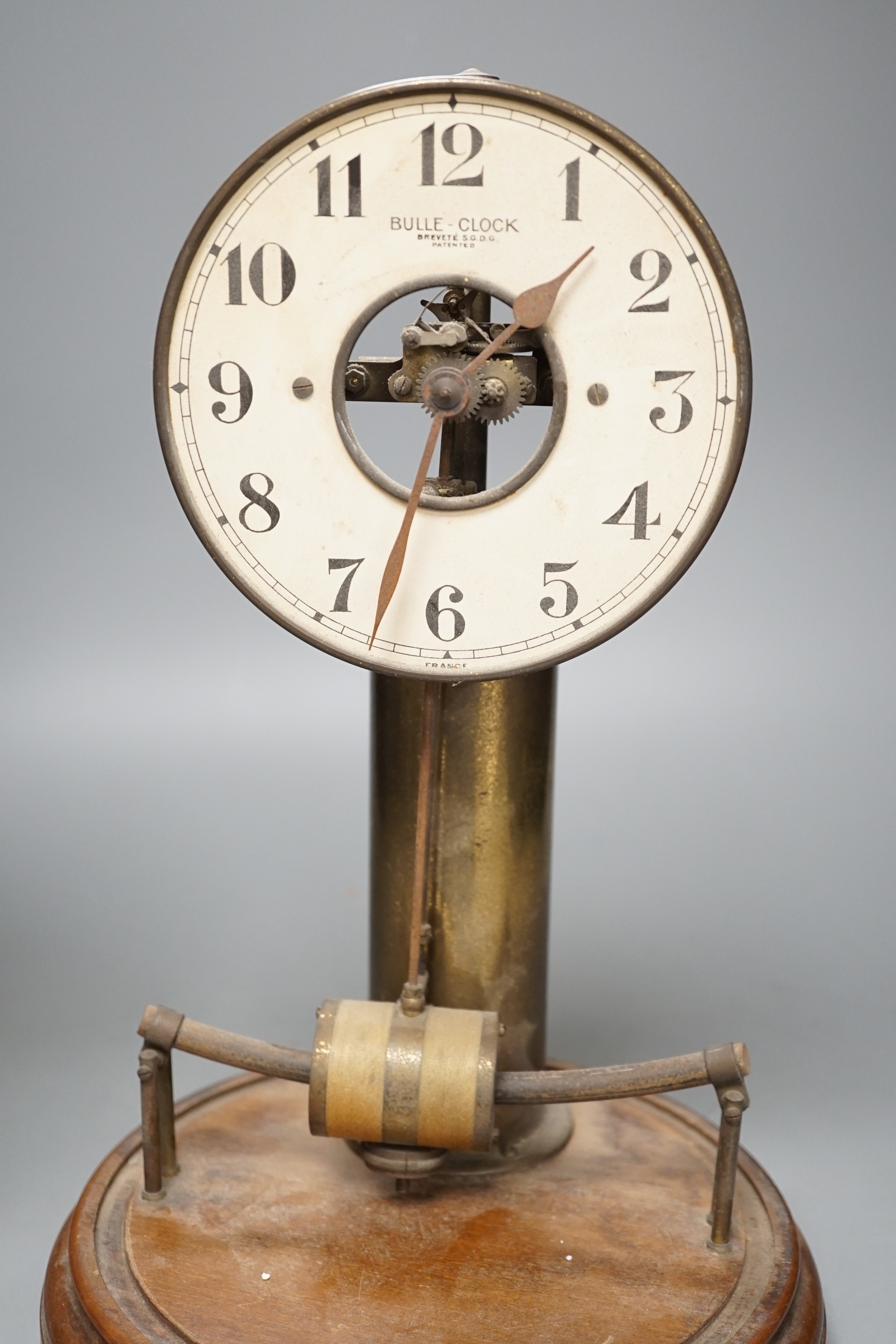 A Bulle electric pendulum clock, with large central brass pillar supporting the 14cm. dial, under a glass dome on a mahogany plinth